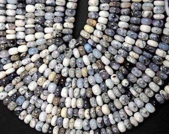 May include: Close-up of a necklace made of oval-shaped beads. The beads are a mix of white, gray, and black, with speckled patterns. The necklace is arranged in a curved shape against a black background.