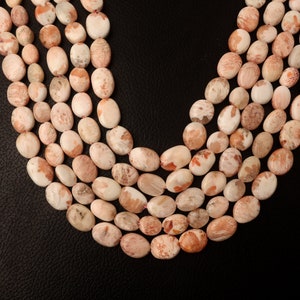 May include: A strand of oval-shaped, pink and white gemstone beads. The beads have a mottled, marbled appearance.