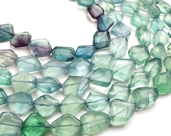 May include: A collection of faceted, irregular gemstone beads in shades of translucent green, blue, and purple. The beads are arranged in multiple strands, showcasing a polished, glassy texture with natural color variations throughout each piece.