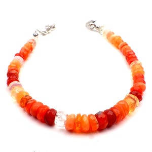 May include: A beaded bracelet featuring a gradient of orange and red gemstones. The bracelet has a silver clasp and is composed of faceted, round beads in shades ranging from pale orange to deep red. The gemstones are strung together to form a flexible band.