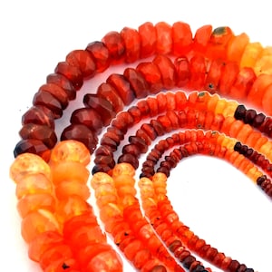 May include: A collection of faceted gemstone beads arranged in multiple strands. The beads display a gradient of warm colors, ranging from deep dark red and brownish-red to vibrant orange, bright tangerine, and pale yellow-orange hues.