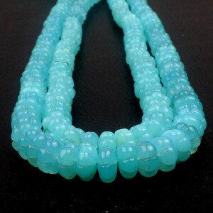 May include: Close-up of a strand of light blue beads. The beads have a textured, carved design and are strung together to form a necklace. The beads are a soft, translucent blue color.