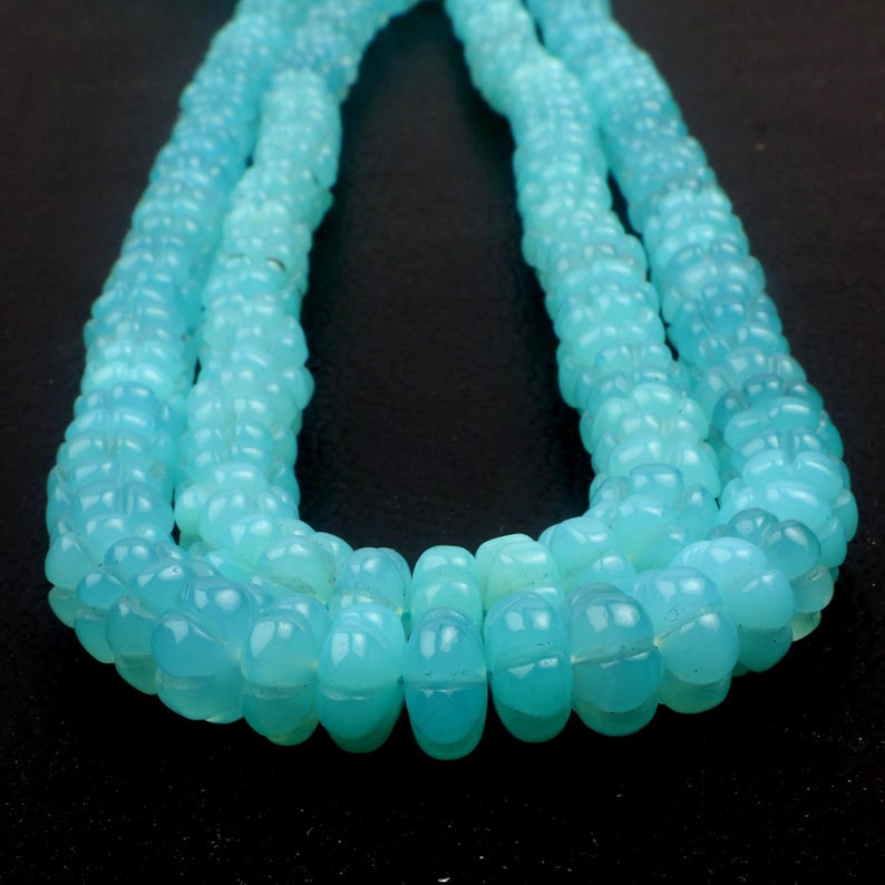 May include: Close-up of a strand of light blue beads. The beads have a textured, carved design and are strung together to form a necklace. The beads are a soft, translucent blue color.