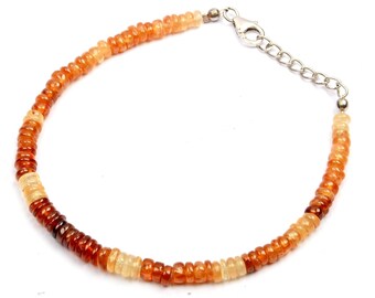 May include: A gemstone bracelet featuring small, round, orange and amber-colored beads. The beads are strung together, creating a continuous loop. The bracelet has a silver-colored clasp and adjustable chain.