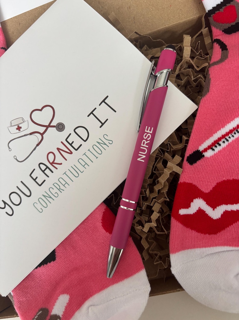 May include: A pink and white pair of socks with a red lip, a stethoscope, and a thermometer design. A pink pen with the word "NURSE" printed on it is included. A card with the text "YOU EARNED IT CONGRATULATIONS" is also included.