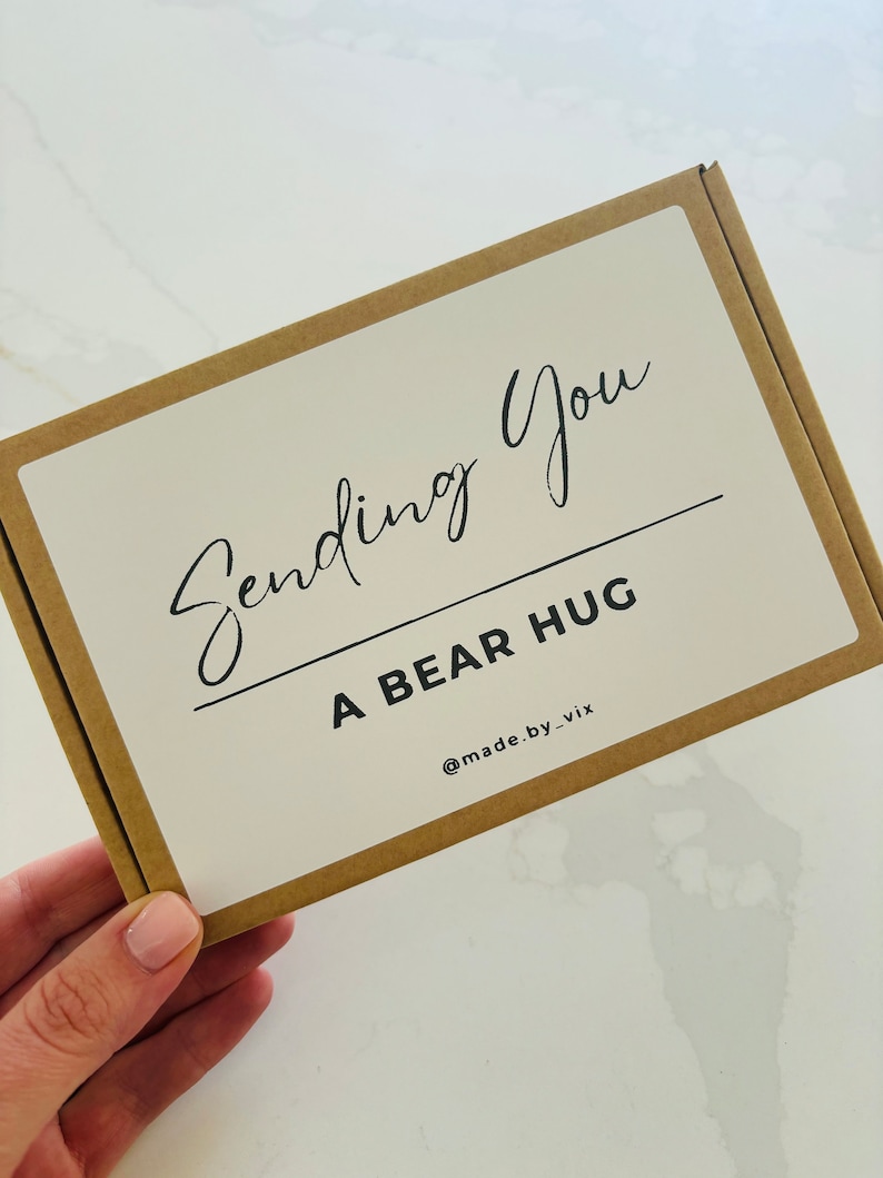 以下が含まれることがあります： 「Sending You A Bear Hug」と「@made.by_vix」と書かれた白いラベルが付いた茶色の段ボール箱です。