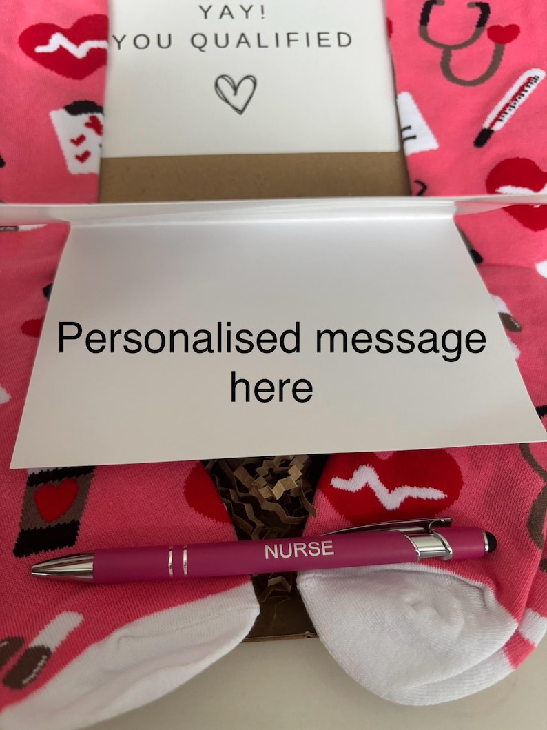 May include: A pink and white pair of socks with a stethoscope, a thermometer, and a heart beat graphic. A pink pen with the word "NURSE" engraved on it. A card with the text "YAY! YOU QUALIFIED" and a heart. A white card with the text "Personalised message here".