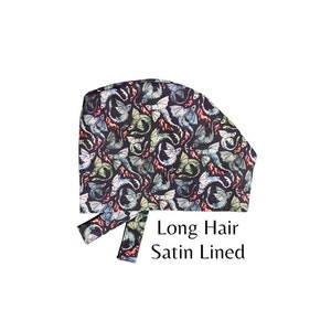 May include: A black scrub cap with a colorful dragon print. The cap is designed for long hair and has a satin lining. The text "Long Hair Satin Lined" is printed on the cap.