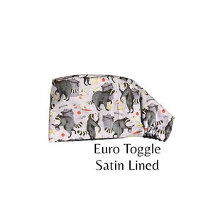 May include: A grey and white scrub hat with a raccoon print. The hat has a euro toggle and is satin lined.