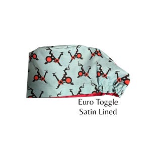 May include: A light blue Euro Toggle satin-lined cap with a repeating pattern of orange and black exercise bikes. The cap has a red trim and the text "Euro Toggle Satin Lined".