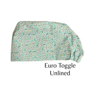 May include: A teal blue surgical scrub hat with a repeating pattern of white and yellow text that says "No Balls Still a Baller". The hat has a euro toggle and is unlined.
