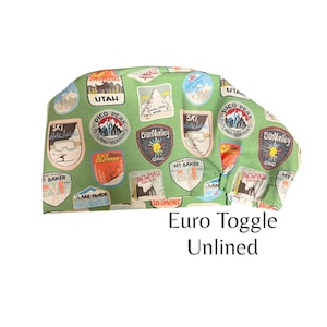 May include: Green fabric with a repeating pattern of colorful vintage ski resort patches. The fabric has the text "Euro Toggle Unlined" printed on it.