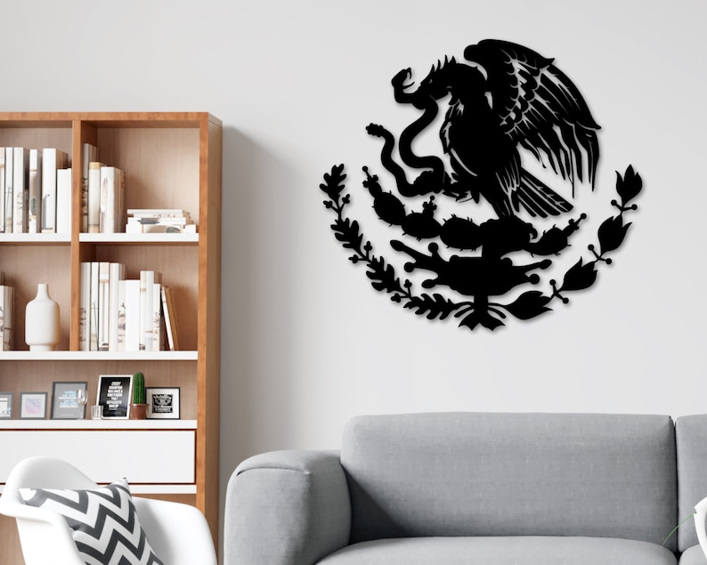 Op de afbeelding: Zwarte metalen wandkunst die het Mexicaanse wapenschild afbeeldt, met een adelaar die op een cactus zit met een slang in zijn bek. De adelaar wordt omringd door een krans van bladeren.