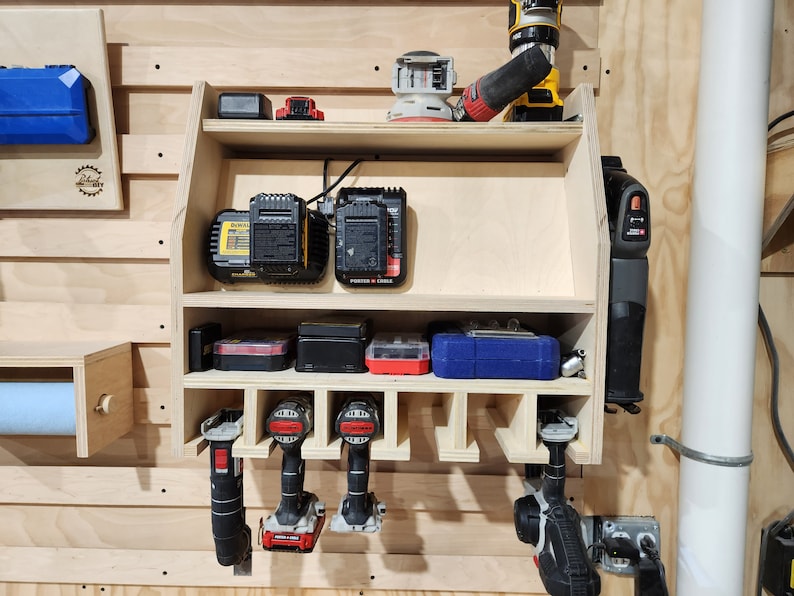 Puede incluir: Un estante de almacenamiento de madera montado en la pared con estantes para herramientas el&eacute;ctricas y bater&iacute;as. El estante tiene ranuras para sujetar taladros y un estante para guardar bater&iacute;as de herramientas. El estante est&aacute; hecho de madera clara y tiene un acabado natural.