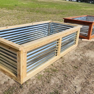 May include: Two rectangular raised garden beds. One is made of natural wood with corrugated metal sides. The other is made of stained wood with corrugated metal sides. Both are outdoors on a dirt surface.