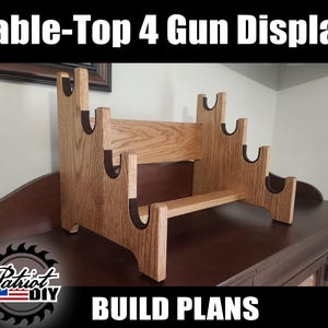 May include: A wooden table-top gun display with four slots. The display is made of light brown wood with dark brown accents. The text "Table-Top 4 Gun Display" and "BUILD PLANS" are at the top and bottom of the image.