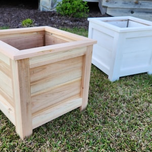 Puede incluir: Dos jardineras cuadradas de madera, una de madera natural y otra pintada de blanco, sentadas en un c&eacute;sped verde.