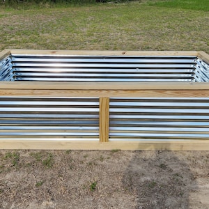 May include: A rectangular raised garden bed with a wooden frame and corrugated metal sides. The natural wood frame surrounds the galvanized metal, creating a rustic look. The bed is designed for planting flowers, vegetables, or herbs.