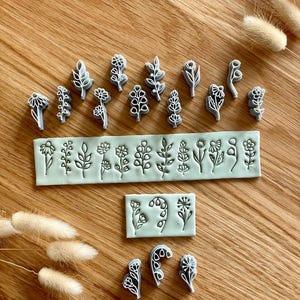May include: A collection of light blue clay stamps featuring various botanical designs, including individual flower and leaf motifs, alongside two rectangular clay slabs embossed with a series of delicate floral patterns in a row.