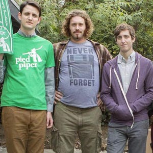 May include: Three men standing in front of a green bush. The man on the left is wearing a green t-shirt with the words "pied piper" on it. The man in the middle is wearing a blue t-shirt with the words "NEVER FORGET" on it. The man on the right is wearing a purple hoodie.