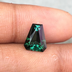 May include: A dark green gemstone with a faceted, triangular shape. The gemstone is cut in a unique, geometric style.