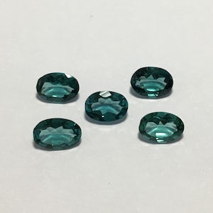 May include: Five oval-shaped teal gemstones with a faceted cut.