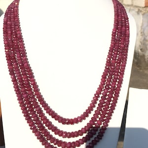 Pode incluir: Um colar de várias voltas feito de contas de rubi vermelho escuro. O colar é exibido em um busto de manequim branco.
