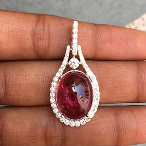 Op de afbeelding: Een hanger met een grote ovale roze edelsteen omringd door een halo van kleinere heldere edelstenen. De hanger is gemaakt van zilver en heeft een delicaat ontwerp.