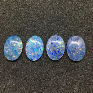May include: Four oval-shaped blue opal cabochons with iridescent shimmer. The opals are arranged in a row on a dark gray background.