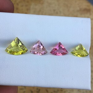 May include: Four triangular cut gemstones, two are yellow-green and two are pink. The gemstones are displayed on a white surface.