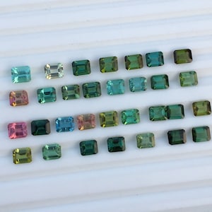 Op de afbeelding: Een assortiment rechthoekige edelstenen in verschillende kleuren, waaronder teal, groen, roze en geel. De edelstenen zijn gerangschikt op een wit oppervlak, waarbij hun gepolijste facetten en levendige tinten worden benadrukt. De edelstenen zijn van verschillende afmetingen.