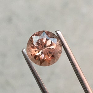 Puede incluir: Una piedra preciosa ovalada de color rosa claro con un patrón en forma de estrella en su interior. La piedra preciosa está sujeta por unas pinzas.
