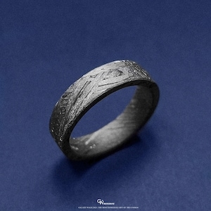 May include: A dark grey ring with a textured surface, set against a blue background. The ring features intricate patterns and designs across its band. The text at the bottom reads "GALAXY WALK 2021 | THE MOST ROMANTIC GIFT OF THE COSMOS."