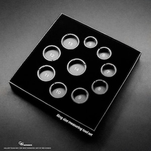 May include: A black ring size measuring tool set with silver-colored ring sizers. The set includes ring sizers numbered 5 through 14. The text "Ring size measuring tool set" is printed on the box.