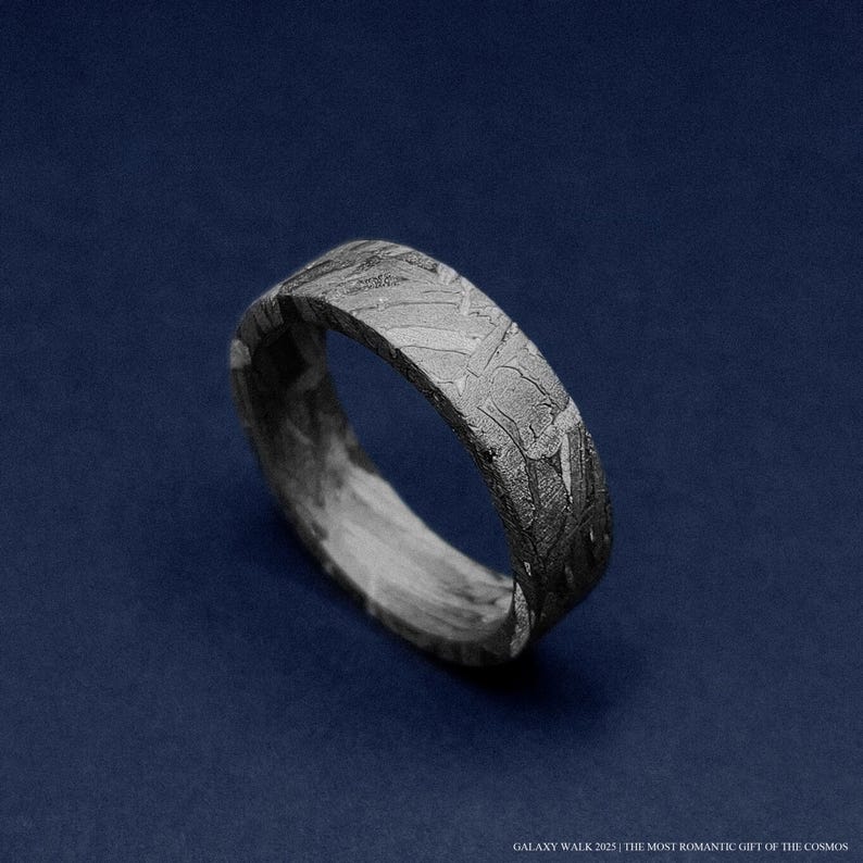K&ouml;nnte beinhalten: Nahaufnahme eines silbernen Rings mit einem einzigartigen, strukturierten Muster. Der Ring hat ein flaches Band und ein dunkles, gesprenkeltes Aussehen. Der Text unten lautet "GALAXY WALK 2025 | THE MOST ROMANTIC GIFT OF THE COSMOS."
