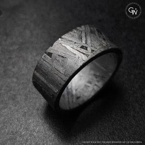 May include: A wide, textured ring with a distinctive pattern. The ring has a dark, metallic appearance with a complex, geometric design across its surface. The ring is set against a dark background. The text "GALAXY WALK 2025 THE MOST ROMANTIC GIFT OF THE COSMOS" is at the bottom.