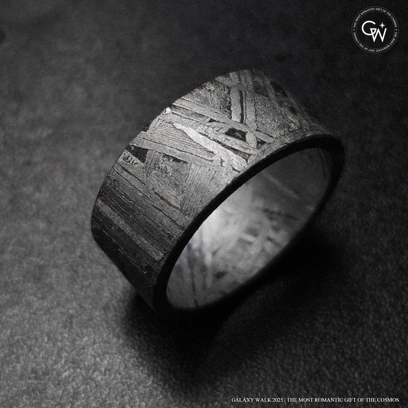 May include: A wide, textured ring with a distinctive pattern. The ring has a dark, metallic appearance with a complex, geometric design across its surface. The ring is set against a dark background. The text "GALAXY WALK 2025 THE MOST ROMANTIC GIFT OF THE COSMOS" is at the bottom.