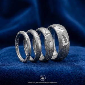 Könnte beinhalten: Vier silberne Ringe mit einzigartigen Mustern werden auf einer blauen Samtoberfläche präsentiert. Die Ringe variieren in der Breite und zeigen komplizierte Designs. Der Text unten lautet "GALAXY WALK | THE MOST ROMANTIC GIFT OF THE COSMOS".