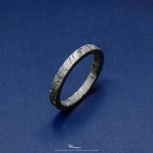 May include: A silver ring with a textured surface, set against a deep blue background. The ring's design features a pattern of diagonal lines, creating a unique appearance. The text at the bottom reads "GALAXY WALK 2023 THE MOST ROMANTIC GIFT OF THE COSMOS."