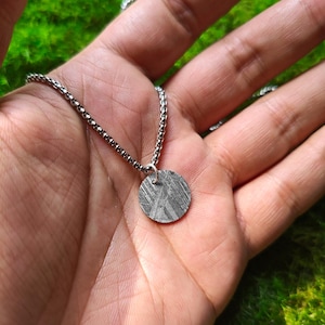 May include: A silver chain necklace with a round, silver pendant. The pendant has a textured surface that resembles a meteorite.