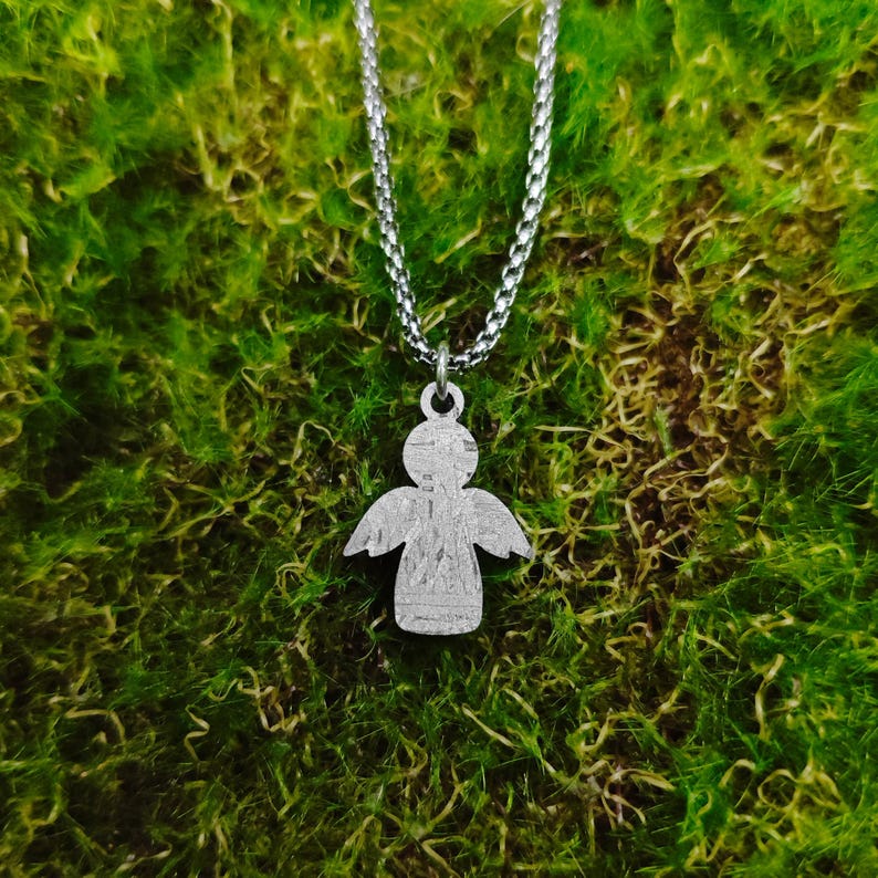 May include: A silver chain necklace with a silver angel pendant. The angel is a simple silhouette with wings and a halo.