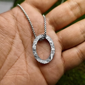 Puede incluir: Un collar de cadena de plata con un colgante ovalado de plata hecho de meteorito. El colgante tiene una superficie texturizada única.