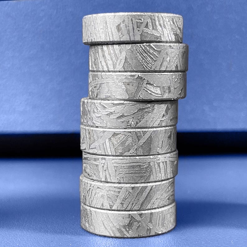 K&ouml;nnte beinhalten: Ein Stapel von sieben silberfarbenen Ringen mit einem einzigartigen, strukturierten Muster. Die Ringe sind zylindrisch und scheinen aus Metall zu sein. Der Hintergrund ist einfarbig blau.