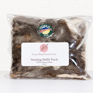 May include: A clear plastic bag containing 3 oz. of raw alpaca fiber in shades of brown, gray, and white. A label reads Crazy Head Creek Farms Nesting Refill Pack 100% Alpaca Fiber 3 oz. A circular sticker states Grown in Montana USA.
