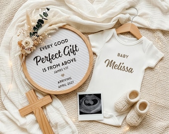 May include: A baby announcement featuring a white onesie with "Baby Melissa" printed on it, a letter board with text, a sonogram, a wooden cross, and knitted baby booties. The letter board says "Every Good Perfect Gift Is From Above".