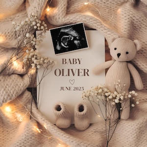 May include: A white card with the text "Baby Oliver June 2025" and a heart symbol. A black and white ultrasound image is in the top left corner. A knitted beige teddy bear is in the top right corner. The card is surrounded by white flowers and a beige knitted blanket.