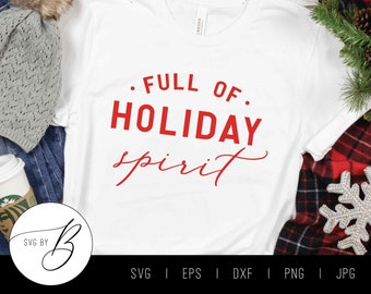 May include: White t-shirt with red text that says "FULL OF. HOLIDAY spirit". The shirt is laying on a blue denim background with a gray knitted hat and a cup of coffee.