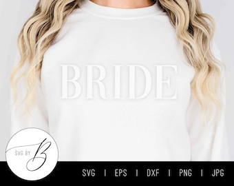 May include: White sweatshirt with the word "BRIDE" printed in white on the front. The sweatshirt is being worn by a person with long blonde hair. A logo with the text "SVG BY" is in the lower left corner of the image.