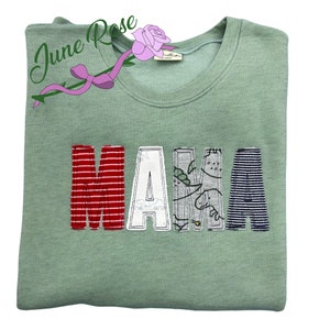 Może przedstawiać: Jasnozielona bluza z napisem "MAMA" wyszytym kolorowymi łatkami z tkaniny. Litery wykonane są z r&oacute;żnych wzor&oacute;w, w tym pask&oacute;w, kropek i nadruku z dinozaurem.