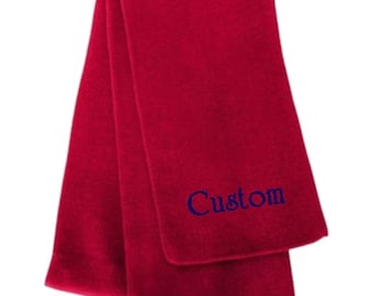 May include: A solid deep red scarf featuring a smooth, soft-textured fabric. The scarf is folded over itself, and the word "Custom" is embroidered in a dark blue, serif-style font on the lower section of the front-facing fabric panel.